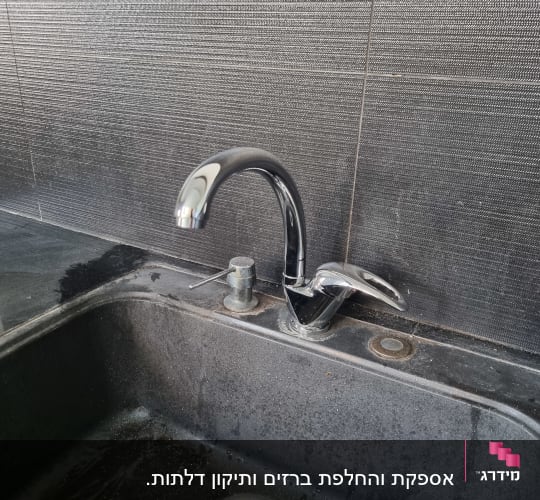 ברז מטבח כסוף מעל כיור שחור עם מים